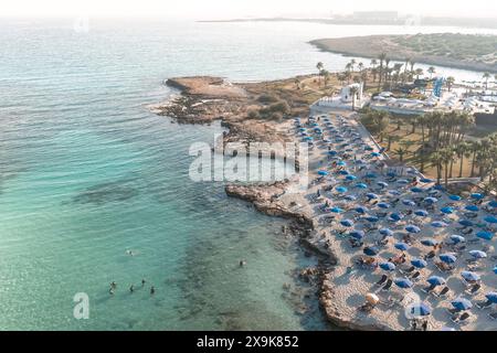 Vue aérienne d'une plage ensoleillée avec des parasols bleus et les gens appréciant la mer. Ayia Napa, Chypre Banque D'Images