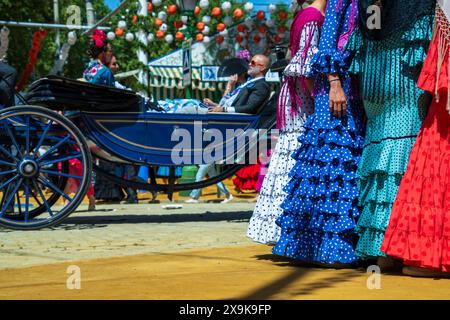 Calèche tirée par des chevaux dans les rues décorées de la Foire d'avril de Séville en Espagne tandis que les femmes en robes de flamenco parlent et apprécient le festival culturel. Banque D'Images