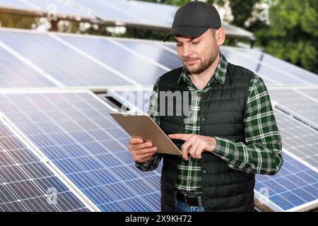 Homme ouvrier de centrale solaire se tient à côté du panneau solaire et travaille sur tablette numérique. Banque D'Images