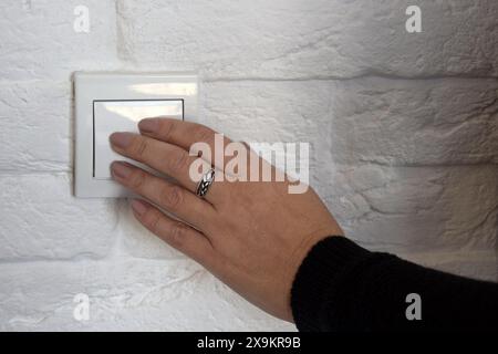 La main femelle pousse le bouton de l'interrupteur blanc sur le mur de briques. Gros plan. Mise au point sélective. Copier l'espace. Banque D'Images