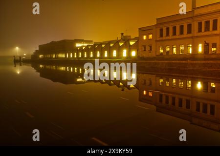 Bâtiment de production avec fenêtres éclairées reflétant dans la rivière calme de nuit Banque D'Images