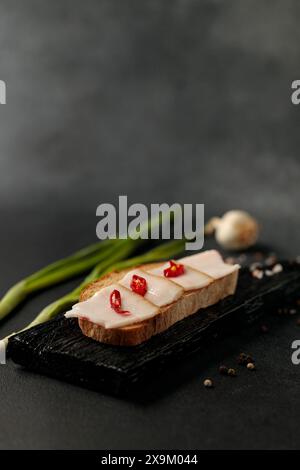 sandwich au saindoux et au poivron rouge sur une planche à découper noire sur fond noir Banque D'Images