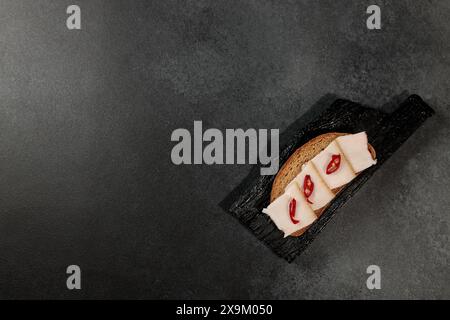 sandwich au saindoux et au poivron rouge sur une planche à découper noire sur fond noir Banque D'Images