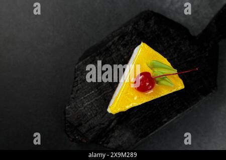 Cheesecake au citron garni de cerises, placé sur un fond noir élégant. Un régal visuel appétissant parfait pour les amateurs de desserts et de plats culinaires Banque D'Images