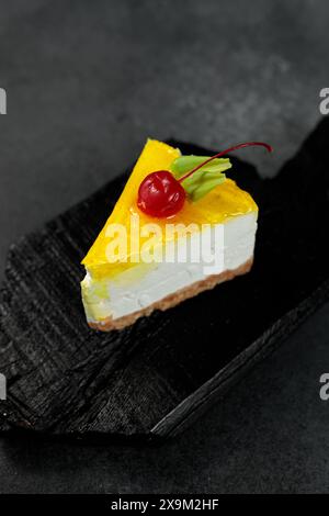 Cheesecake au citron garni de cerises, placé sur un fond noir élégant. Un régal visuel appétissant parfait pour les amateurs de desserts et de plats culinaires Banque D'Images