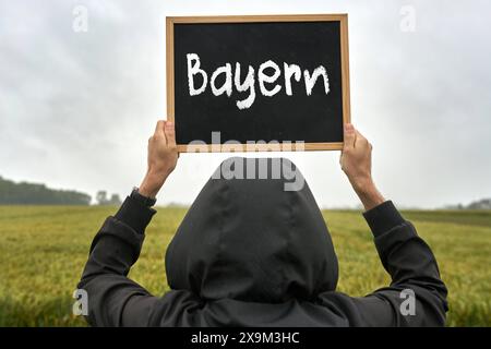 1er juin 2024 : un homme en tenue de pluie tient une plaque dans l'air sous la pluie avec l'inscription : Bavaria. PHOTOMONTAGE *** Ein Mann in Regenkleidung hält eine Tafel in die Luft BEI Regen mit Aufschrift : Bayern. FOTOMONTAGE Banque D'Images