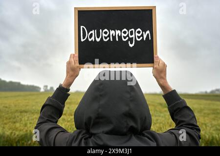 1er juin 2024 : un homme en tenue de pluie tient une plaque dans l'air sous la pluie avec l'inscription : pluie continue. PHOTOMONTAGE *** Ein Mann in Regenkleidung hält eine Tafel in die Luft BEI Regen mit Aufschrift : Dauerregen. FOTOMONTAGE Banque D'Images