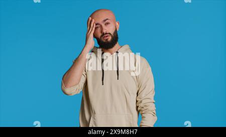 Homme musulman souffrant de migraine grave sur la caméra, essayant de frotter les temples pour soulager la pression. Jeune adulte du moyen-Orient se sentant mal avec mal de tête douloureux, personne malade. Caméra 1. Banque D'Images