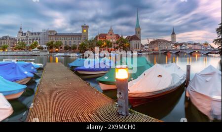 Vue panoramique du quai de Zurich sur la rivière Limmat avec des bateaux et Fraumunster au crépuscule, Suisse Banque D'Images