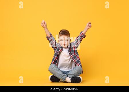 Heureux petit garçon assis sur fond jaune Banque D'Images