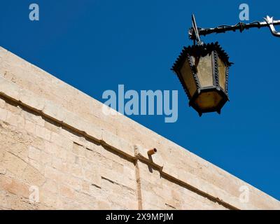 Une ancienne lanterne est accrochée à un mur de pierre contre un ciel bleu profond, la ville de mdina sur l'île de malte avec des maisons historiques, des balcons colorés Banque D'Images