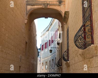 Une ruelle étroite entre des bâtiments historiques avec des murs de pierre et des volets rouges, couverte par une arche, la ville de mdina sur l'île de malte avec Banque D'Images