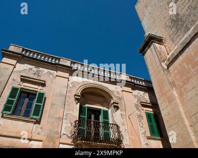 Façade d'un ancien bâtiment avec volets verts et balcon décoratif, la ville de mdina sur l'île de malte avec des maisons historiques, colorées Banque D'Images