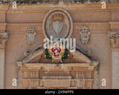 Un blason détaillé sur un vieux mur de pierre, entouré d'ornements et de reliefs, la ville de mdina sur l'île de malte avec des maisons historiques Banque D'Images