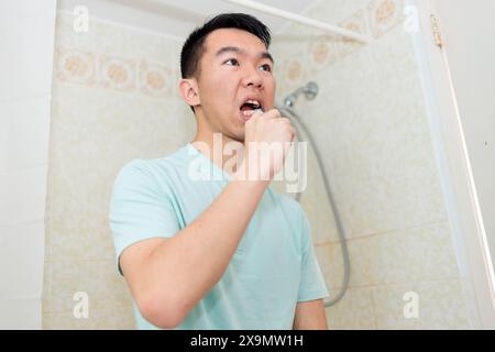 Dans une salle de bain, un jeune adolescent utilise une brosse à dents pour nettoyer ses dents. Banque D'Images