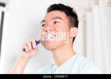 Un jeune adolescent se tient devant un miroir, se brossant les dents. Il effectue sa routine matinale dans la salle de bain. Banque D'Images