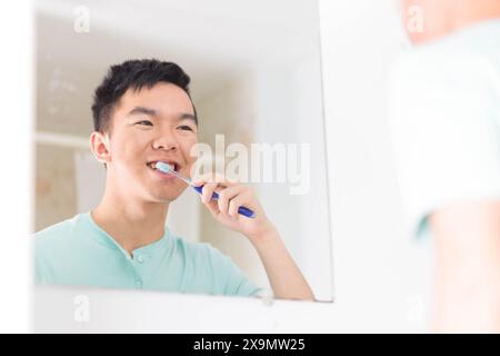 Un jeune adolescent se tient devant un miroir, se brossant les dents dans le cadre de sa routine quotidienne matinale Banque D'Images