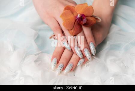 Une capture rapprochée révèle une main de personne avec des ongles floraux complexes berçant délicatement une fleur d'oranger. La texture douce et bouffante environnante Banque D'Images