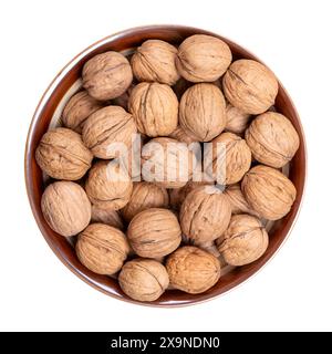 Noix dans leurs coquilles, dans un bol brun. Graines séchées non décortiquées du noyer commun Juglans regia. Noix entières avec coquilles, utilisées comme snack etc Banque D'Images