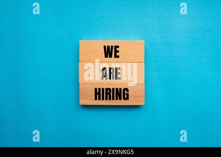 Nous embauchons des mots écrits sur un bloc de bois avec un fond bleu. Conceptuel, nous embauchons symbole. Copier l'espace. Banque D'Images