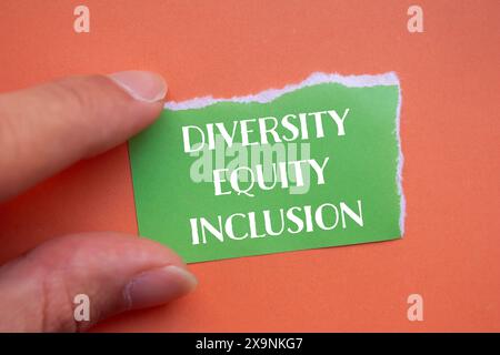 Mots sur la diversité, l'équité et l'inclusion écrits sur un papier vert déchiré avec un fond orange. Diversité conceptuelle, équité et inclusion DEI symbo Banque D'Images