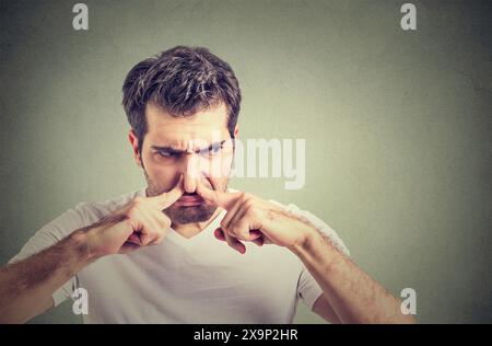 Jeune homme portant un t-shirt blanc décontracté sentant quelque chose de puant et dégoûtant, odeur intolérable, retenant le souffle avec les doigts sur le nez Banque D'Images