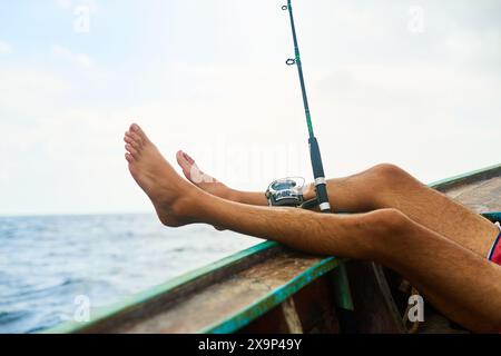 Homme, pieds et bateau pour la pêche dans l'océan avec détente, vacances avec activité aquatique pour le bien-être. Personne masculine, jambes vers le haut et la mer avec la rupture de coulée sur le navire Banque D'Images