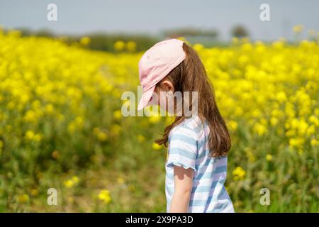 Petite fille dans un champ de fleurs jaunes. Fille dans un chapeau Banque D'Images