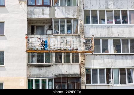 Un homme est debout sur un échafaudage attaché au côté d'un bâtiment, surveillant le paysage urbain. L'immeuble semble être une propriété résidentielle Banque D'Images