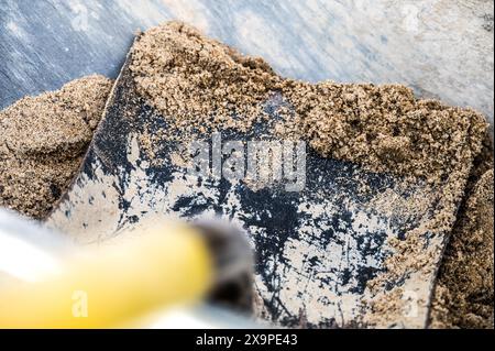 Vue détaillée d'une pelle en métal rouillé soulevant le sable, mettant en évidence les contrastes de texture entre la rouille et le sable frais. Idéal pour la construction ou le jardinage th Banque D'Images