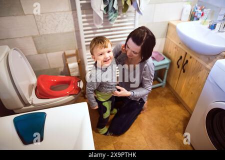 Maman aide le tout-petit garçon à utiliser les toilettes. Petit garçon formé au pot dans la salle de bain. Banque D'Images