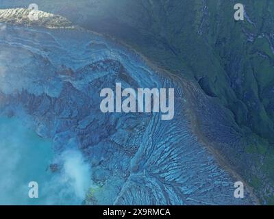 Vue aérienne à couper le souffle de la majestueuse chaîne de montagnes du cratère du volcan Ijen avec brouillard, lac clair, ciel réfléchissant, forêts verdoyantes Banque D'Images