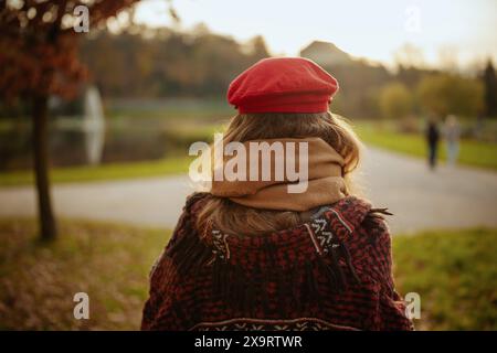 Bonjour l'automne. Vu de derrière femme en chapeau rouge avec foulard marchant dans le parc de la ville. Banque D'Images