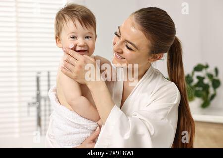 Mère heureuse appliquant une crème hydratante sur le visage de bébé dans la salle de bain Banque D'Images