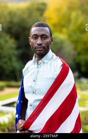 Portrait d'homme afro-américain sérieux couvert de drapeau des usa dans le jardin Banque D'Images