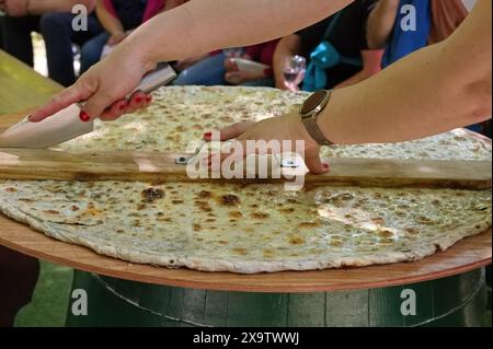 Womans Hands Cut soparnik - cuisine croate traditionnelle sur une grande assiette en bois Banque D'Images