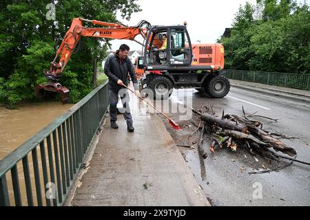 Meckenbeuren Brochenzell, Allemagne. 03 juin 2024. Un homme balaie le sentier piétonnier sur un pont qui traverse la rivière Schussen, tandis qu'à l'arrière-plan une excavatrice est prête à enlever le bois brisé de la rivière Schussen. Le Schussen avait inondé des parties de Meckenbeuren. Crédit : Felix Kästle/dpa/Alamy Live News Banque D'Images