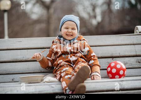Mignonne jeune fille mangeant le déjeuner dans le parc, assise sur le banc. Pique-niquez dans le parc pendant la froide journée de printemps. Banque D'Images