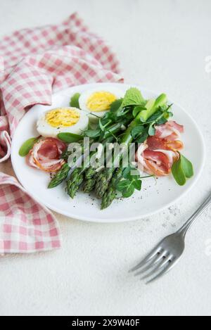 Une salade saine composée de lances d’asperges vertes, de prosciutto finement tranché et de moitiés d’œuf à la coque, garnies de feuilles fraîches de microgreens, Banque D'Images