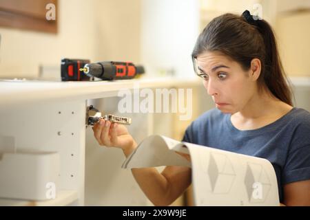 Femme perplexe lisant le manuel d'assemblage des meubles dans la cuisine Banque D'Images