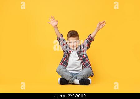 Heureux petit garçon assis sur fond jaune Banque D'Images