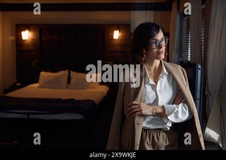 Femme d'affaires joyeuse réussie regardant rêveur à la fenêtre dans la chambre d'hôtel Banque D'Images