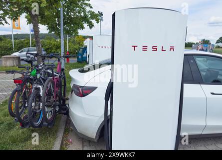 Voiture électrique Tesla avec porte-vélos sur l'attelage de remorque à une centrale électrique Tesla Super charger dans une station-service d'arrêt d'autoroute à Schwabach, Allemagne, le 27 mai 2024. Banque D'Images