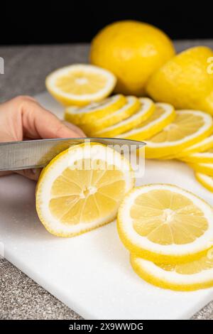 Femme coupant le citron en tranches avec un couteau utilitaire pointu sur une planche de cuisine en pierre. Banque D'Images