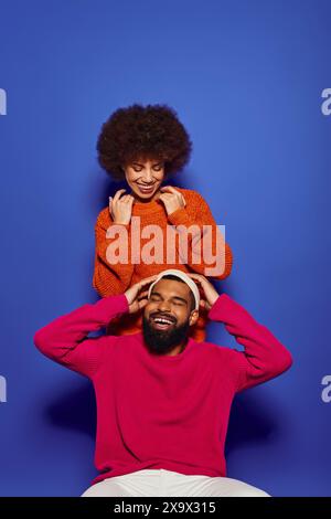 Un jeune homme afro-américain est assis sur une tête de femme dans une tenue décontractée vibrante, montrant l'amitié. Banque D'Images