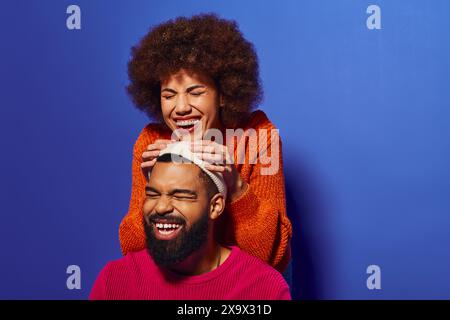 Jeune homme et femme afro-américains en tenue vibrante riant ensemble, mettant en valeur l'amitié et la camaraderie. Banque D'Images