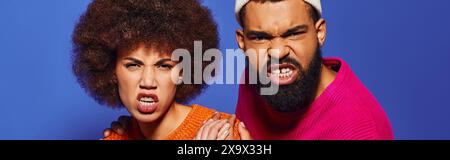 Un jeune homme et une femme afro-américains en tenue vibrante, exprimant des émotions sur un fond bleu. Banque D'Images