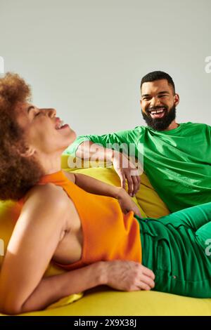 Un homme et une femme, heureux amis afro-américains, s'inclinant sur une chaise de sac de haricots dans des vêtements vibrants, symbolisant l'amitié. Banque D'Images