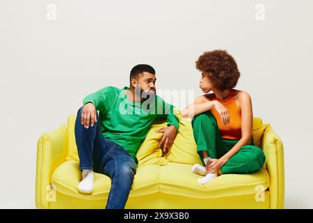 Heureux amis afro-américains dans des vêtements vibrants assis sur un canapé jaune, mettant en valeur l'amitié entre l'homme et la femme. Banque D'Images Heureux amis afro-américains dans des vêtements vibrants assis sur un canapé jaune, mettant en valeur l'amitié entre l'homme et la femme. Banque D'Images