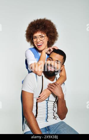 Un homme afro-américain tient une femme sur ses épaules, montrant la force et l'amitié dans des vêtements élégants sur un fond gris. Banque D'Images